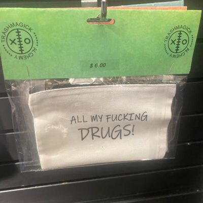 White zippered pouch with bold black lettering that reads: “ALL MY FUCKING DRUGS!” Mounted on a green Trashmagick Alchemy header card with $6.95