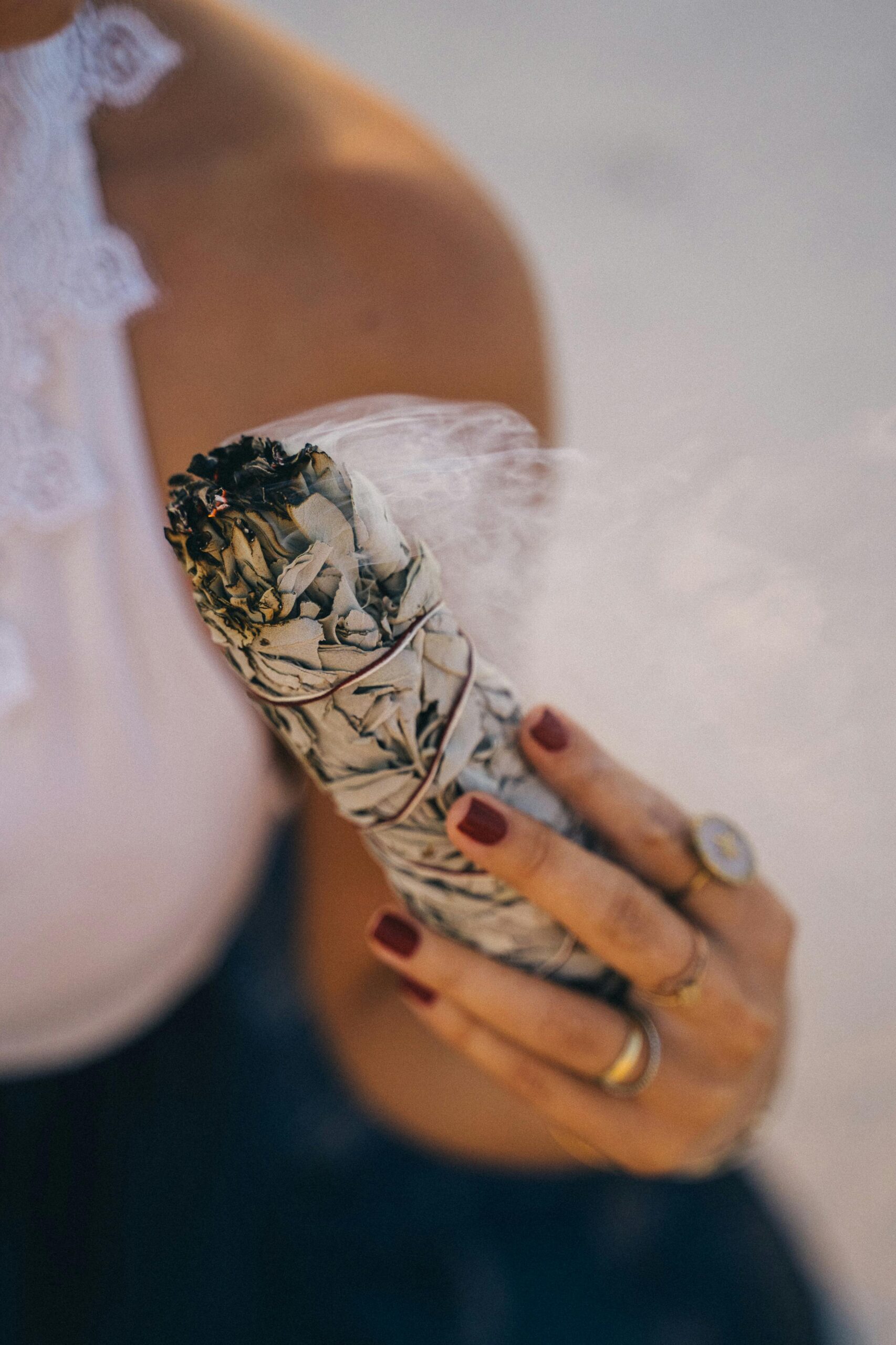 Close-up of a woman holding a burning sage stick for spiritual cleansing outdoors.